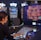 A person is seated at a slot machine console in a casino, focusing intently on the game displayed on the screen. The background shows several other illuminated gaming machines, adding a vibrant and colorful atmosphere to the scene.